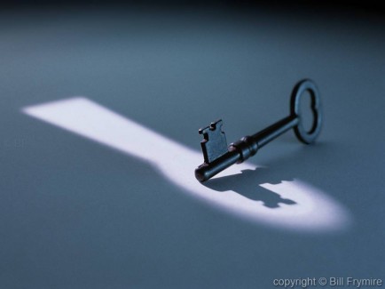 a lone key in spotlight of a keyhole making a shadow