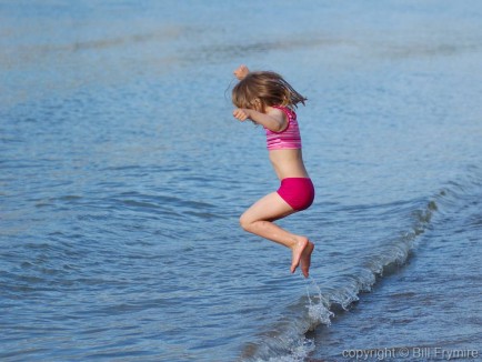 young girl jumping waves at the water's edge