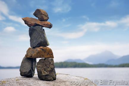 Inukshuk sitting on a rock by the ocean
