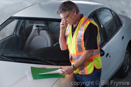 Man Wearing Safety Vest Standing by Car using Cell Phone <br />