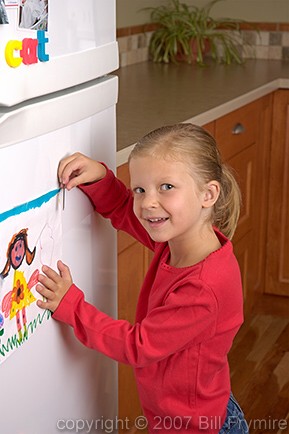 girl putting drawing on fridge door