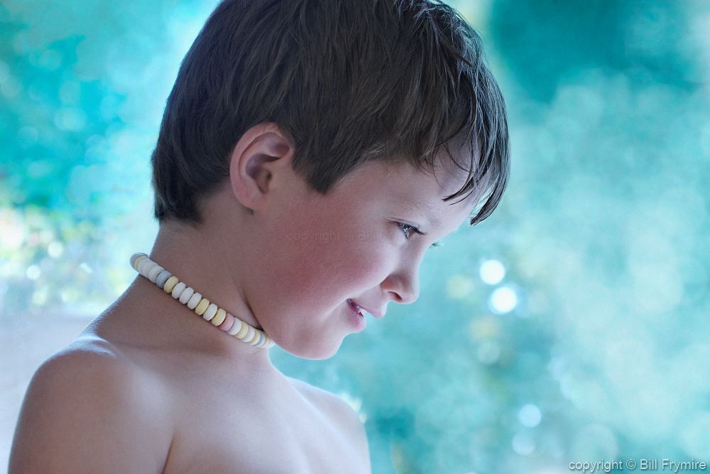 This is a photograph of a young boy in profile with a smile on his face and...