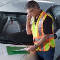 Man Wearing Safety Vest Standing by Car using Cell Phone <br />