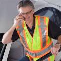 Man Wearing Safety Vest Standing by Car using Cell Phone <br />